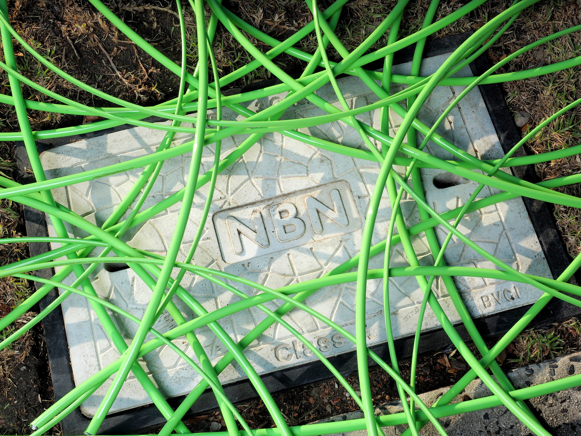 Green NBN fiber-optic cable in an unstructured condition over a pit with a utility hole cover displaying the NBN word mark in Melbourne, Australia.